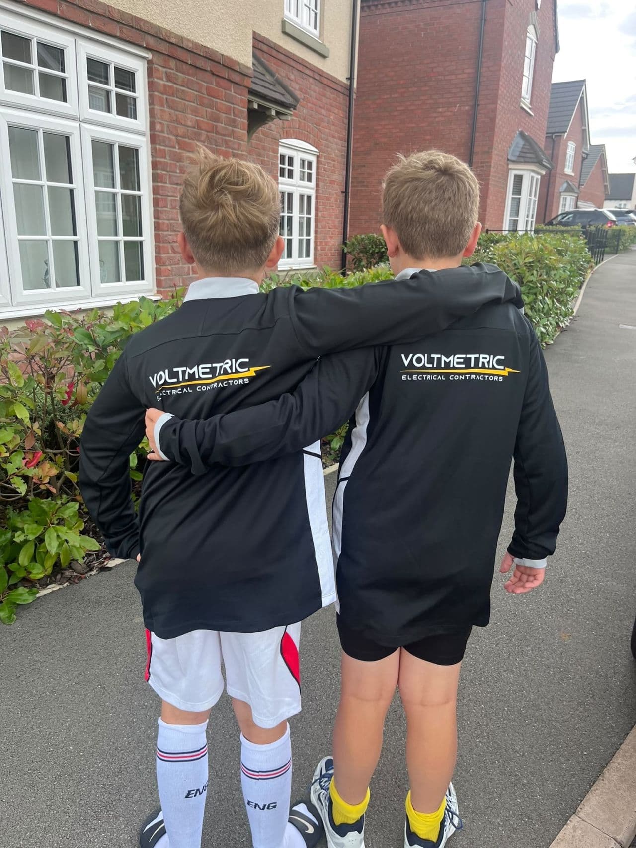 Two Harborough Town U10s players from behind, wearing black training tops with the Voltmetric Electrical Contractors logo.